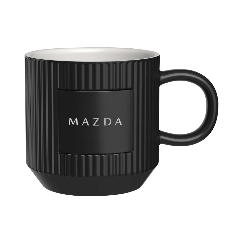 A black ceramic mug with a ribbed design, featuring a black center panel with the white 'MAZDA' logo. The mug has a white interior and a black handle, shown against a plain white background.